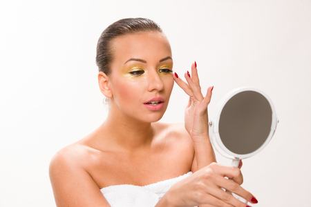 Gold make up. Brown sleek hair beautiful woman looking at mirror.の写真素材