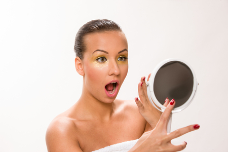 Gold make up. Brown sleek hair beautiful woman looking at mirror.の写真素材