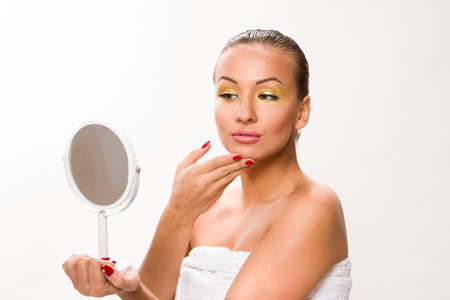 Gold make up. Brown sleek hair beautiful woman looking at mirror.の写真素材