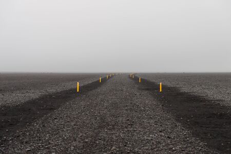 Iceland volcanic gravel road with yellow road markers in foggy day