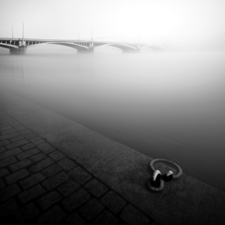 Foggy autumn mood at Vltava river. Reflection of bridge in water. Detail of riverbank. Black and white atmosphere, Prague, Czech republicの写真素材
