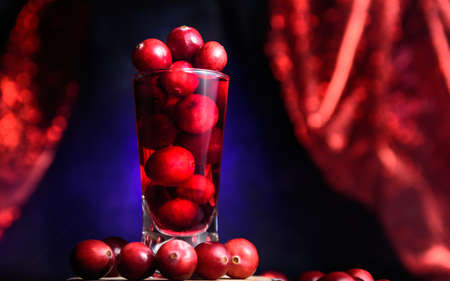 Red cranberies presented in theatrical scenery with red curtain around dark blue background. Shot full of vitamins and microelements important for staying healthy and strong. Immunity suport system.の写真素材