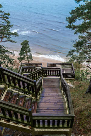 Old mossy wooden stairs leading from the forest to sandy beach. Wet weather. Green evergreen trees leading to baltic sea side.の写真素材