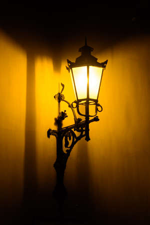 Modern electric street lamp build in victorian style street lamp at night. Deep yellow light produced to illuminate night streets.の写真素材