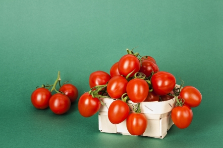 Small tomatoes in the basket shown on a green backgroundの写真素材