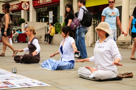 LONDON - JUNE 05: Three women meditating in yoga pose on a small square in the center of the city are of interest for passers-by in London in England on June 05, 2010のeditorial素材