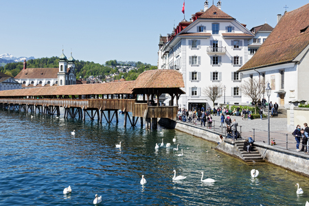 LUCERNE, SWITZERLAND - MAY 05, 2016: Entry to roofed wooden the Chapel Bridge that connects the two banks of the river Reuss can be seen on the right side of the riverのeditorial素材