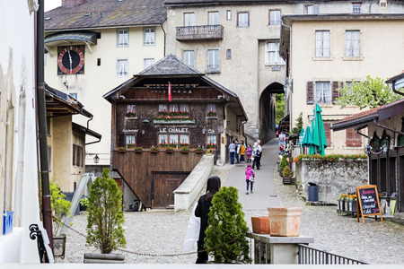 GRUYERES, SWITZERLAND - MAY 25, 2013: Narrow gate, timber house, townhouses and some people watching something on both sides of the street it all can be seen at the end of the main square of this cityのeditorial素材
