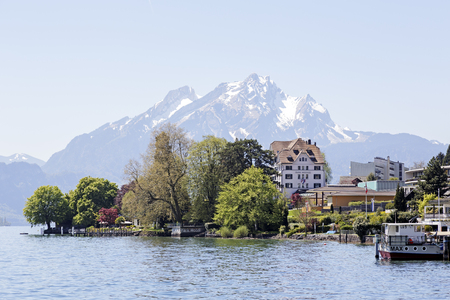 WEGGIS, SWITZERLAND - MAY 05, 2016: Trees and buildings on the shore of Lake Lucerne and in the distance the snow-capped Mount Pilatus. The scenic area is a popular destination for tourist tripsのeditorial素材