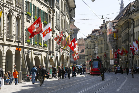 Bern, Switzerland - April 20, 2017: Townhouses and visible flags along the street on which you can...