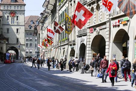Bern, Switzerland - April 20, 2017: Traffic in a city where there are many pedestrians and a tram in the distance. The street is decorated with flags that are placed on facades of buildingsのeditorial素材
