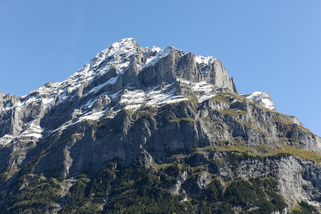 Alpine mountain peak as seen from Grindelwald.  The rocky mountains cliffs, snow covered peaks and slopes covered with greenery can be seenの写真素材
