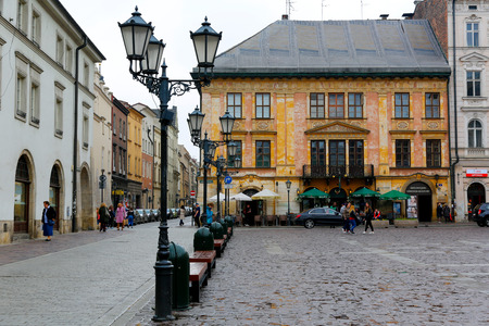Krakow, Poland - May 25, 2017: Historic building with decorative facade is visible on the edge of The Small Market Square. There is a cobbled street, street lamps, cars parked and people who walkのeditorial素材