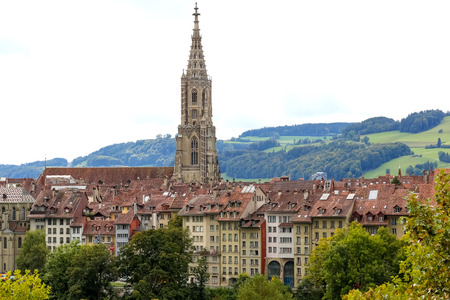 Bern, Switzerland - September 18, 2017: The tower of the cathedral dominates over other residential buildings of the old town. In the distance there are meadows and forests on the hill.のeditorial素材
