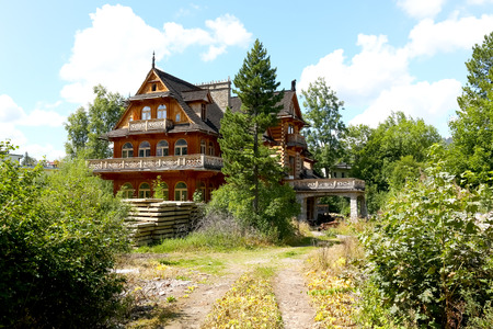 Zakopane, Poland - August 14, 2017: The old large wooden villa, slightly hidden in the greenery, looks like deserted and awaiting renovation. The roof of this house is covered with a wooden shingle.のeditorial素材