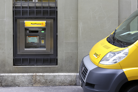 Bern, Switzerland - February 19, 2018: The ATM machine was placed by the street and built into the front wall of the building. A postal vehicle stopped next to it.のeditorial素材