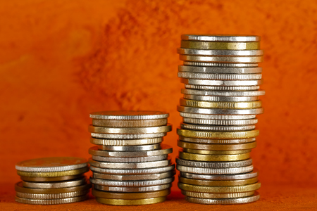 There are various coins stacked in three stacks and are visible against orange backgroundの写真素材