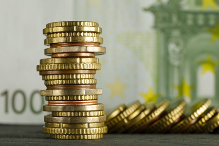 Various Euro coins visible against background of one banknote of on hundred Euro