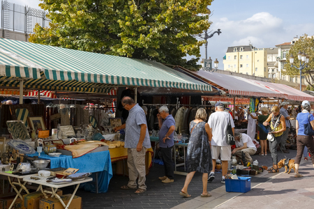 Nice, France - September 24, 2018: People walk and watch various items on sale during the business day at Cours Saleya. Above the stalls there are canvas roofs made of striped material.のeditorial素材