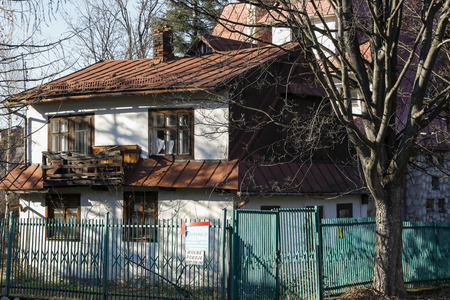 Zakopane, Poland - November 17, 2018: The old house is behind the fence and next to it grows a large tree. The roof of this residential building is covered with metal sheets.のeditorial素材