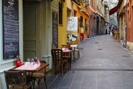 Nice, France - September 18, 2018: Narrow street between tenement houses. There are three tables and a few chairs, it is quite empty around, but there are a few people in the distance.のeditorial素材