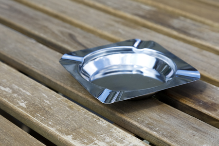A metal empty ashtray was placed on a wooden table.の写真素材