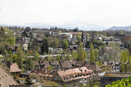 Bern, Switzerland - April 22, 2019: General view of the city with houses and trees that grow between the buildings. The Alpine mountain range is seen at a distance.のeditorial素材