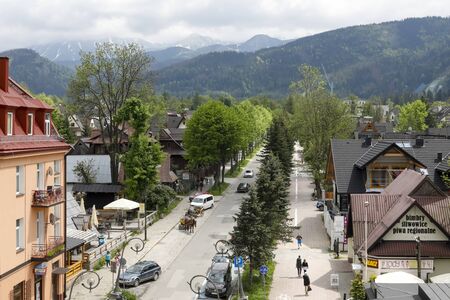 Zakopane, Poland - June 01, 2019: Aerial view of the street leading to the mountains. There are buildings, many trees and there are several tourists watching the cityのeditorial素材