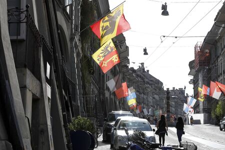 Bern, Switzerland - April 22, 2019: There are many various flags illuminated by the sun. The facades...