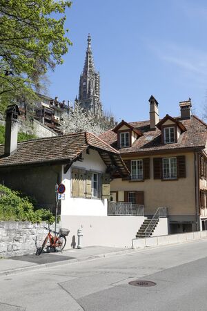 Bern, Switzerland - April 18, 2018: Traditional residential buildings. The massive cathedral tower...