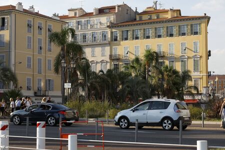 Nice, France - September 17, 2018: Behind the street there are tenement houses with windows equipped with shutters. Cars have stopped on the street, there are a few people in the distance.のeditorial素材