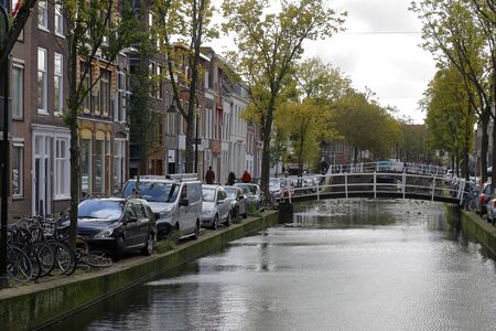 Delft, The Netherlands - October 10, 2019: Trees growth nearby the canal and also there are cars parked along the bank. Small bridges connects the two banks of the canal.のeditorial素材