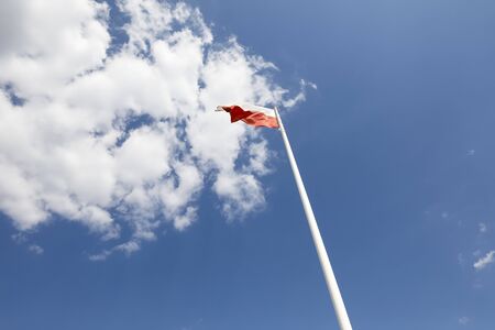 One flag of Poland is seen during the a windy day. There is the background of the blue sky and white cloudsの写真素材