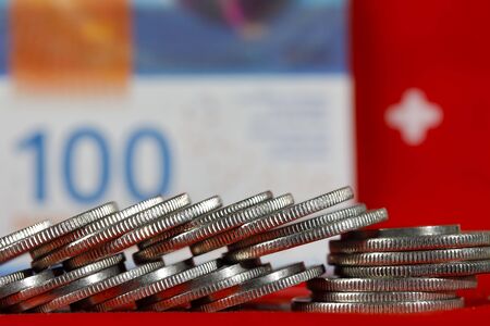A group of Swiss coins and in the background is a banknote and the symbol of the Swiss flag.