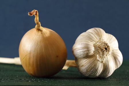 One onion and one garlic are on a dark, painted, wooden surface.の写真素材