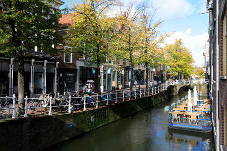Delft, The Netherlands - October 10, 2019: There is an inland waterway canal in the city. There are residential buildings along this canal and an outdoor restaurant on a moored barge is located.のeditorial素材