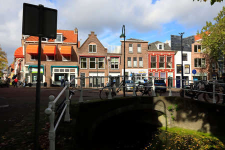 Delft, The Netherlands - October 10, 2019: A view of the sunlit buildings in the city. The stone bridge connecting the canal banks remains in the shade.のeditorial素材