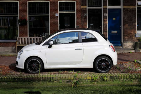 Delft, The Netherlands - October 10, 2019: A car, Fiat 500 in the narrow street parked between brick...