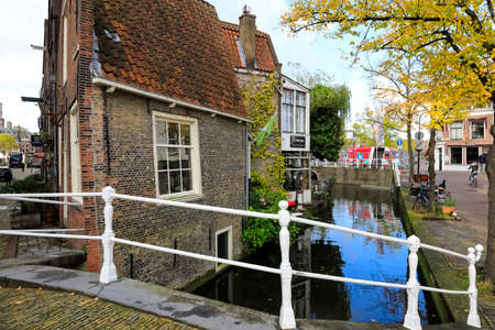 Delft, The Netherlands - October 10, 2019: A bridge providing a passage over the inland waterway from where the old brick house can be observed.のeditorial素材