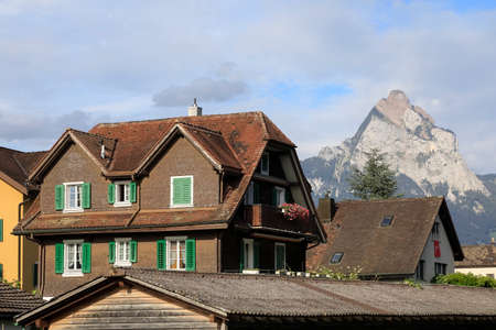 Brunnen, Switzerland - August 27, 2020: There is a house with slanted roof and with green shutters and there are other rooftops as well. The huge Grosser Mythen in a background is seen on a sunny day.のeditorial素材