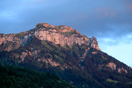 Against the blue sky, in the evening, the top of one of the many mountains in the Swiss Alps is visible. The rays of the setting sun painted the rocks the colors of the evening.の写真素材