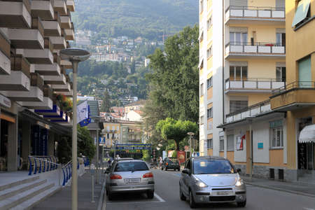Locarno, Switzerland - July 13, 2009: There is a little traffic on narrow city street that leads between apartment buildings. Many residential houses are on a hill visible in a distance.のeditorial素材