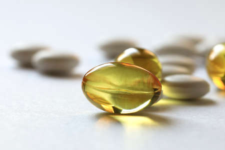 Tablets and capsules are scattered on the surface of white paper. These are medical products of different medicinal use.の写真素材