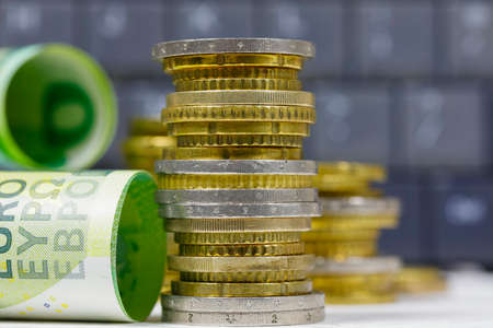 A group of Euro banknotes and Euro coins stacked next to each other against a dark background of a computer keyboard, EUR currencyの写真素材