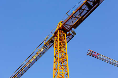 Warsaw, Poland - December 21, 2021: Two construction cranes working on the construction site in the Goclaw housing estate. There crane booms are visible against the sunny blue skyのeditorial素材