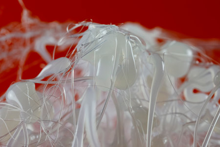 Drops and strands of hot glue have already cooled down and are visible against a red backgroundの写真素材
