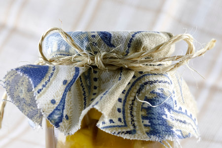 A glass jar with preserves topped with a piece of cloth and rolled up with a twine.の写真素材