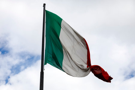 The national flag of Italy is placed at the top of the flagpole and there it waves in the wind and is visible against a cloudy sky in Florence, Italy.の写真素材