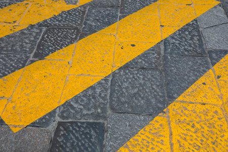 Yellow stripes on a black cobbled street mark a pedestrian crossing somewhere in Florence, Italy.の写真素材