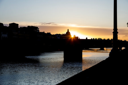 Landscape scenery of summer sunset over old bridge, which spans the Arno river. Bridge and buildings silhouette can be seen against colorful sunset sky of city of Florence in Italyの写真素材